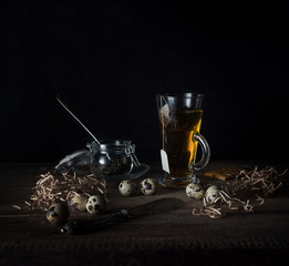 rustic still life. cup of tea and quail eggs on a wooden table. black background.