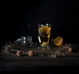 rustic still life. cup of tea, lemon and quail eggs on a wooden table. black background