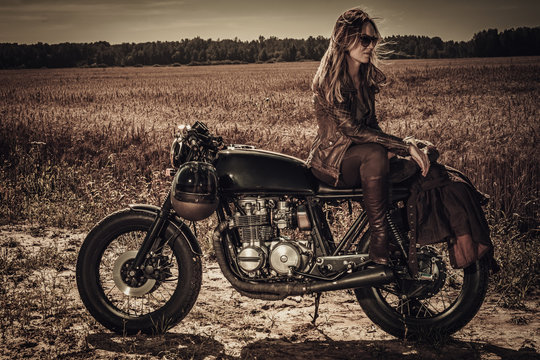 Young, stylish woman on vintage custom cafe racer in field
