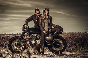 Junges, stylisches Café-Racer-Paar auf alten Custom-Motorrädern im Feld