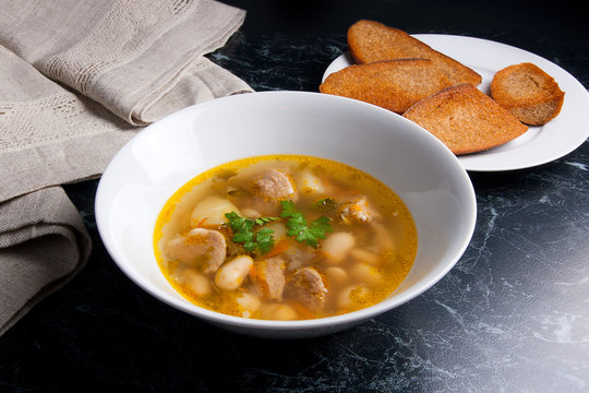 Bean soup in white plate, several toast on white plate on a blac
