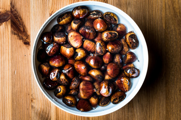 Chestnuts in white bowl on wooden surface.
