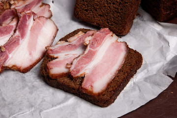 Puff smoked bacon with rye black bread on the packaging paper. V