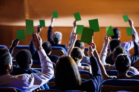 Rear view of business executives show their approval by raising hands at conference center