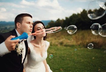 beautiful and young bride and groom inflating bubbles outdoors