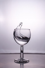 Transparent glass cup with a pouring bubbling cold fresh water with bubbles and drops