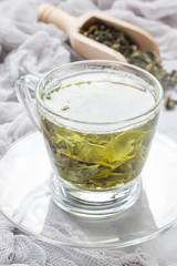 Cup of fresh made green tea, dry leaves on background, vertical