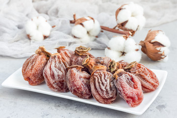 Several dried persimmon on white plate, gray concrete background, horizontal