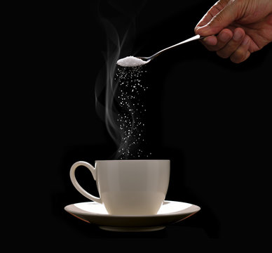 Hand putting sugar in coffee cup with smoke on black background