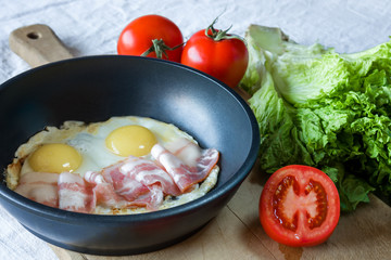 Scrambled eggs and bacon on frying pan on table close-up