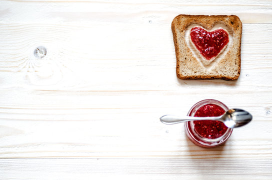 Toasted white bread, in which the heart of raspberry jam. Under the croutons is a jar of jam. In a jar lies a small spoon.