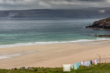 North Coast, Scotland - June 6, 2012: Line of multi-colored laundry hangs above Durness Beach, a sandy patch looking north on a rough coast among rock cliffs and sprinkled pieces of rock.
