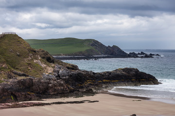 Fototapeta na wymiar North Coast, Scotland - June 6, 2012: Cliffs descend on Durness Beach, a sandy patch looking north on a rough coast among rock cliffs and sprinkled pieces of rock.