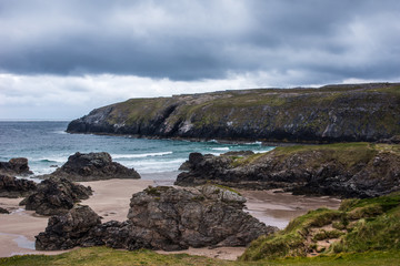 North Coast, Scotland - June 6, 2012: Cliffs descend on Durness Beach, a sandy patch looking north on a rough coast among rock cliffs and sprinkled pieces of rock.