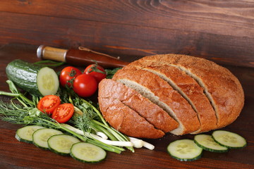 Каравай ржаного хлеба и  овощи лежат на столе на темном деревянном фоне. Деревенский стиль.