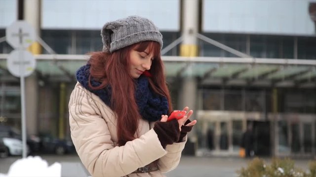 Young hipster girl with smartphone typing sms on street and smile into camera. Lifestyle concept.