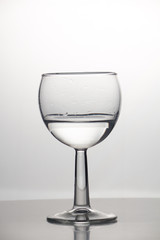 Transparent glass cup with a pouring bubbling cold fresh water with bubbles and drops