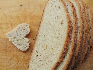 Foto auf Glas Herzförmiges Stück Brot vor Vollbrot © melih2810