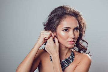 Young woman with make-up and styling tries on beautiful earrings. Gray background.