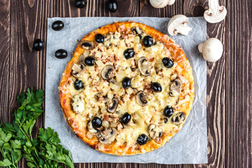 Pizza with meat, mushrooms, pineapple and olives on a wooden background