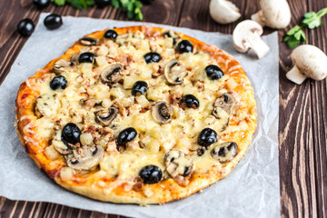 Pizza with meat, mushrooms, pineapple and olives on a wooden background