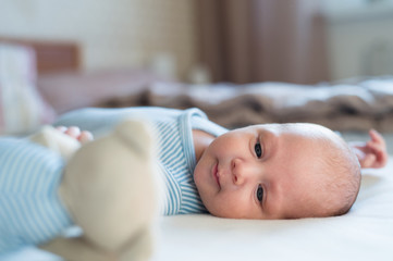 Cute newborn baby boy with teddy bear lying on bed