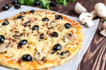 Pizza with meat, mushrooms, pineapple and olives on a wooden background