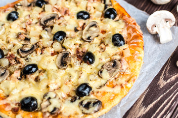 Pizza with meat, mushrooms, pineapple and olives on a wooden background