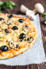 Pizza with meat, mushrooms, pineapple and olives on a wooden background