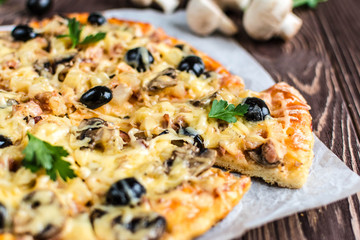 Pizza with meat, mushrooms, pineapple and olives on a wooden background