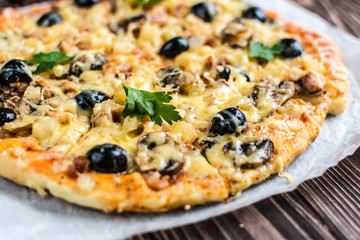 Pizza with meat, mushrooms, pineapple and olives on a wooden background