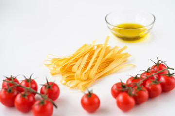 Uncooked italian pasta, olive oil and tomatoes cherry on a white