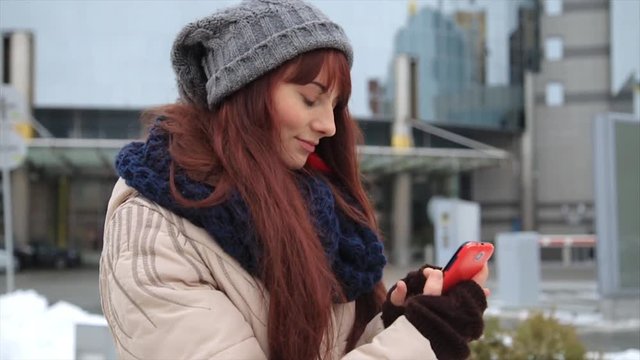 Young hipster girl with smartphone typing sms on street and smile into camera. Lifestyle concept.