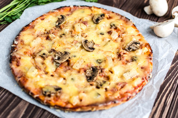Hawaiian pizza with meat, mushrooms and pineapple on a wooden background