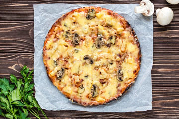 Hawaiian pizza with meat, mushrooms and pineapple on a wooden background