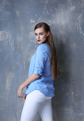 Portrait of young beautiful woman in blue shirt on grey background