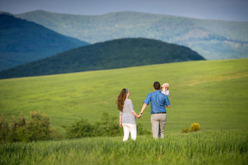 Young family on a walk against green fields and hills