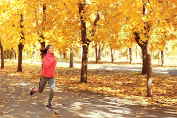 Sporty young woman running in autumn park