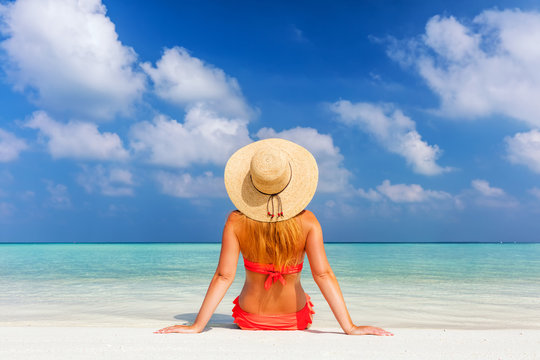 Beautiful young woman in sunhat sitting relaxed on tropical beach in Maldives