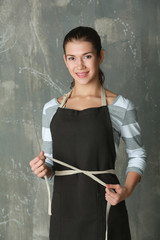 Woman tying apron on color background