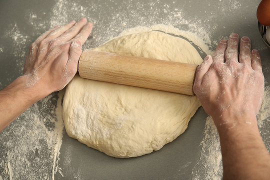 Man rolling out dough on kitchen table, close up