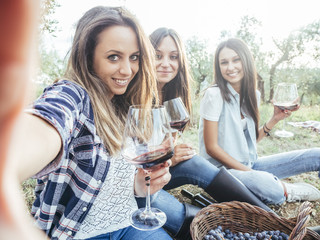 Three girlfriends take selfie in a field while drinking red wine after the grape harvest