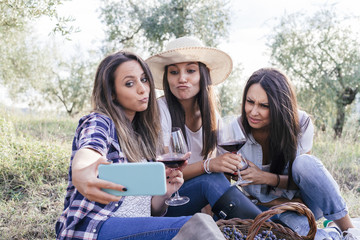 Three girlfriends take selfie in a field while drinking red wine after the grape harvest