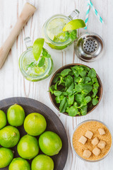 Two fresh mojitos cocktail in mason jar on wooden background. Mojitos with mint leaves, lime and ice. Drink making tools and ingredients for cocktail. View from above.