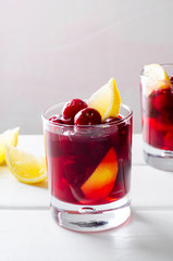 Cold drink with cherry and lemon in glasses, on white wooden background