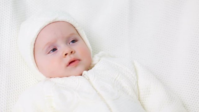 baby girl knitted in white overalls lying on the bed