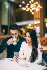 Young couple sitting at cafe drinking coffee and using mobile phone
 