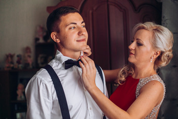 Naklejka premium Mother is helping with a bow-tie to her son before wedding ceremony. Concept mother and son.