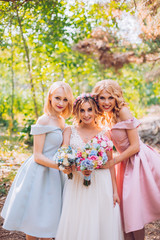 Obraz na płótnie Canvas Amazing blond girls. Bride with bridesmaids with flowers hand in medow sunny pine forest.
