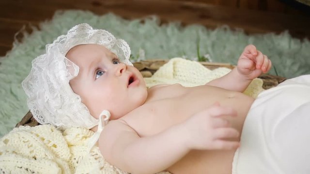 girl kid naked in a white cap lying in the basket and looks at parents
